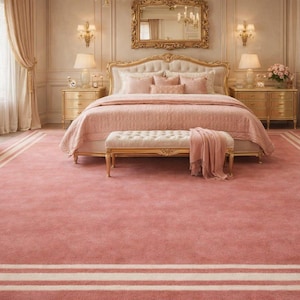 Puede incluir: Un dormitorio lujoso con una cama grande, un banco y una alfombra. La cama está cubierta con ropa de cama rosa, y la alfombra es rosa a juego con rayas blancas. La habitación tiene detalles dorados, incluyendo un espejo y muebles.