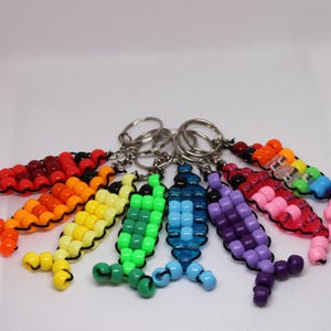 May include: A collection of seven beaded fish keychains in a rainbow of colors. Each keychain features a fish design made of small, colorful beads strung together, with a silver keyring attached.