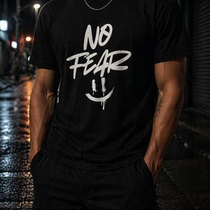 以下が含まれることがあります： 「NO FEAR」の白文字と、滴るスマイリーフェイスのデザインが施された黒いTシャツ。半袖のシャツは黒いズボンと組み合わされています。シルバーのチェーンが見えます。夜間の屋外で撮影された画像です。