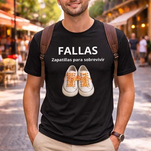 May include: Black t-shirt with the word "FALLAS" and the phrase "Zapatillas para sobrevivir" printed in white. The shirt features a graphic of white sneakers with orange laces. The person is wearing a brown backpack.