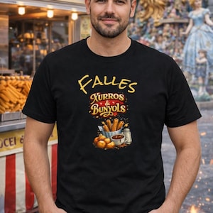 May include: Black t-shirt featuring the words "Falles Xurros & Bunyols" in yellow script. The design includes illustrations of churros, bunyols, and dipping sauce. A food stand with the words "Xurros Buñuelos" is visible in the background.