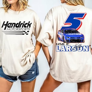 May include: Cream-colored t-shirt featuring the "Hendrick Motorsports" logo in black on the front. The back displays a blue race car graphic with the number 5 and "Kyle Larson" text in blue and white.