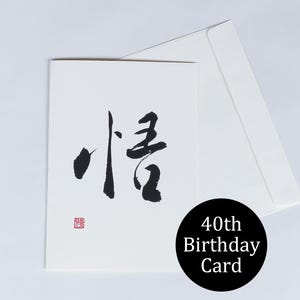 以下が含まれることがあります： 白い誕生日のカード。黒い書道と赤いスタンプが特徴です。白い封筒も写っています。右下には「40th Birthday Card」と書かれた黒い円があります。