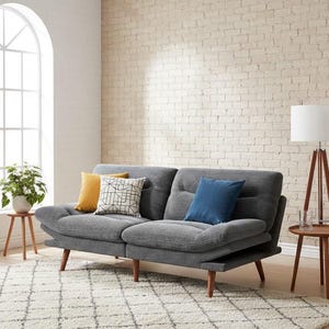 May include: A gray corduroy sofa with wooden legs, adorned with colorful throw pillows. The sofa sits on a patterned rug in a room with a brick wall and a large arched window. A floor lamp and side table are also present.