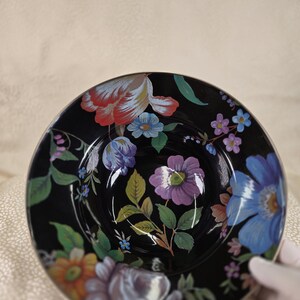 May include: A black ceramic bowl with a floral pattern. The bowl is decorated with colourful flowers in red, blue, purple, and orange, with green leaves. The flowers are set against a black background.