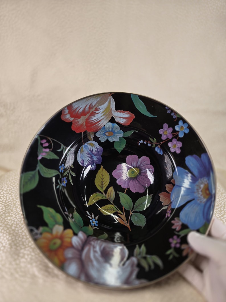 May include: A black ceramic bowl with a floral pattern. The bowl is decorated with colourful flowers in red, blue, purple, and orange, with green leaves. The flowers are set against a black background.