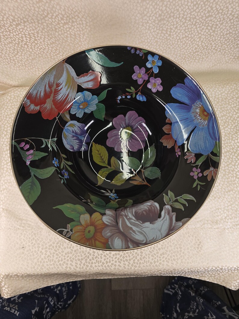 May include: A black ceramic bowl with a floral pattern. The bowl displays colourful flowers in shades of red, blue, purple, and yellow. The rim has a gold trim. The bowl is likely used for serving food.