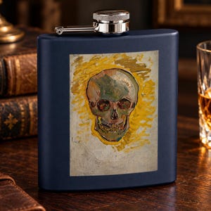 May include: A dark blue metal flask featuring a rectangular print of a human skull with a yellow halo-like background. The flask has a polished silver-tone screw-top cap with a hinged arm attached to the neck of the container.