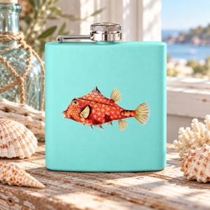 May include: A light turquoise metal flask featuring a detailed illustration of a red fish with a white star pattern on its body. The flask has a silver-colored screw-top cap with a hinged arm mechanism attached to the top of the rectangular container.