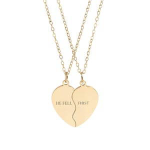 May include: Two gold-colored necklaces with heart-shaped pendants. Each pendant forms half of a heart, with a split down the middle. One pendant reads "HE FELL" and the other reads "FIRST". The necklaces have delicate chain links.