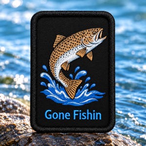 May include: A rectangular black embroidered patch featuring a brown and white trout jumping out of blue water splashes. The text "Gone Fishin" is embroidered in light blue letters at the bottom of the patch, which has a thick black border.