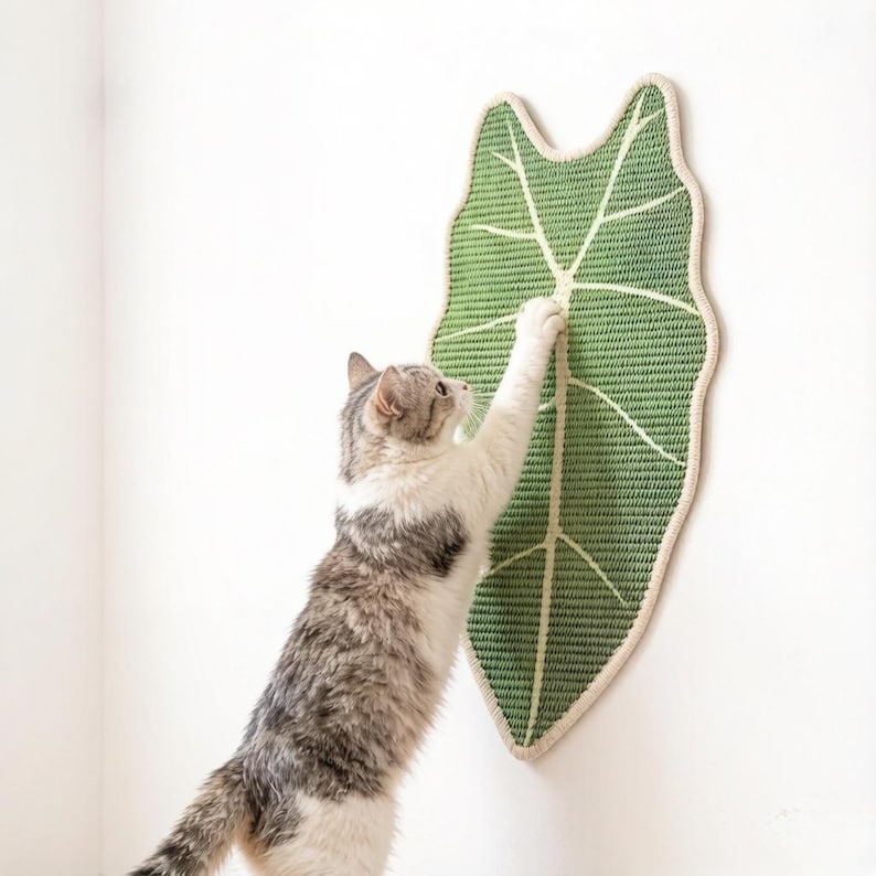 K&ouml;nnte beinhalten: Ein an der Wand montiertes Kratzbrett f&uuml;r Katzen in Form eines gro&szlig;en gr&uuml;nen Blattes mit cremefarbenem Rand und markanten cremefarbenen Blattadern. Die strukturierte Oberfl&auml;che ist zum Kratzen gedacht und hat ein Webmuster.