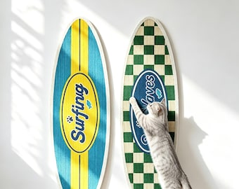 Puede incluir: Dos rascadores para gatos con forma de tabla de surf. El de la izquierda es azul y amarillo con el texto "Surfing" en un óvalo amarillo. El de la derecha presenta un patrón de cuadros verdes y blancos con un óvalo azul con el texto "Waves".