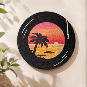 Puede incluir: Una pieza de arte mural circular dise&ntilde;ada como un disco de vinilo. El centro presenta una vibrante escena de atardecer con la silueta de una palmera negra, un cielo naranja y rosa, y un sol amarillo reflejado sobre un oc&eacute;ano dorado.
