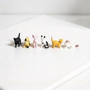 Könnte beinhalten: Ein Set aus sechs Miniatur-Katzenfiguren in verschiedenen Posen und Farben, darunter eine einfarbig schwarze Katze, eine gelb gefleckte Katze, eine weiß-rosa Katze, eine schwarz-weiße Katze, eine einfarbig orange Katze und eine weiß-braune Langhaarkatze.