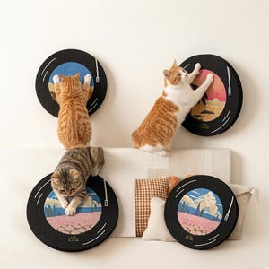 Puede incluir: Cuatro rascadores circulares para gatos dise&ntilde;ados como discos de vinilo, con anillos exteriores negros, gr&aacute;ficos de brazo fonocaptor blancos y etiquetas centrales ilustradas con paisajes, con dos gatos rascando las superficies.
