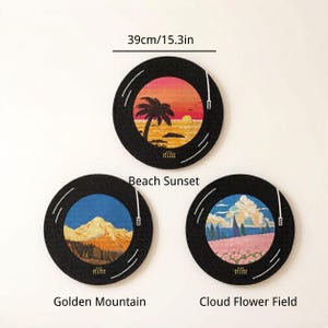 Puede incluir: Tres decoraciones de pared circulares de 39 cm de di&aacute;metro, dise&ntilde;adas como discos de vinilo. Los dise&ntilde;os muestran una puesta de sol en la playa, una monta&ntilde;a dorada y un campo de flores con nubes. Cada pieza tiene un borde negro con l&iacute;neas blancas.
