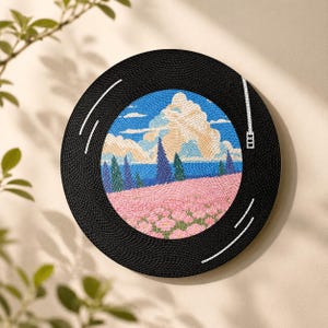 Puede incluir: Una pieza de arte mural circular dise&ntilde;ada para parecer un disco de vinilo negro. El centro presenta una ilustraci&oacute;n de paisaje texturizada y detallada de un campo de flores rosas, &aacute;rboles azules altos y un cielo azul con nubes blancas.