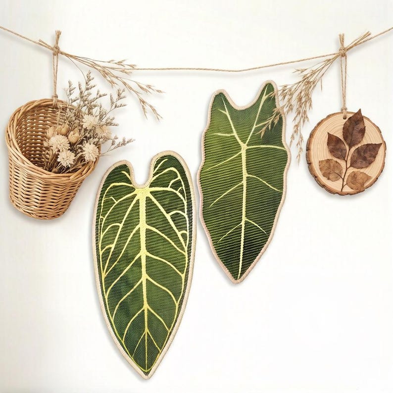 K&ouml;nnte beinhalten: Ein Wandbehang-Set bestehend aus einem kleinen geflochtenen Weidenkorb mit Trockenblumen, zwei stoffartigen blattf&ouml;rmigen Wanddekorationen mit dunkelgr&uuml;nem und gelbem Adernmuster sowie einem runden Holzscheiben-Ornament mit braunem Blatt.