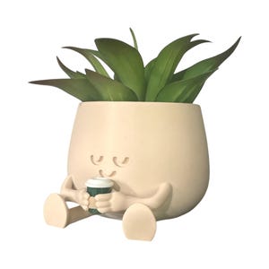 May include: A whimsical, cream-colored planter shaped like a relaxed figure, holding a small coffee cup. The planter features a smiling face and attached legs and arms. It is filled with green, leafy faux succulents.