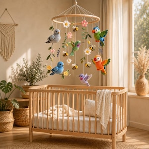 May include: A hanging nursery mobile featuring crocheted figures of various birds, including a blue bird, a green hummingbird, and colorful parrots, interspersed with crocheted bees, white and pink flowers, and green leaves suspended from a wooden ring.