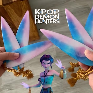 May include: A figurine of a woman in a teal and blue outfit, holding two pairs of stylized, wing-shaped objects. The objects are painted with a gradient of blue, pink, and white. The text "K-POP DEMON HUNTERS" is visible.