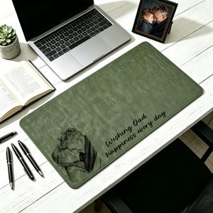 Può includere: Un tappetino verde per scrivania con un'immagine stampata di una coppia e la scritta "Wishing Dad happiness every day". Un laptop, penne e una foto incorniciata sono anche sulla scrivania bianca.