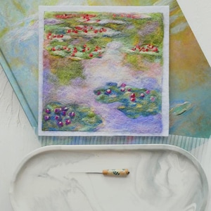 May include: A square needle felted textile art piece depicting a water lily pond with green lily pads and small red and purple flowers. Below the artwork sits a white oval marble-patterned tray holding a single metal needle felting tool.