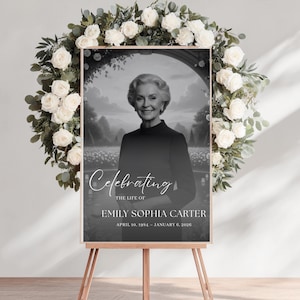 Könnte beinhalten: Ein schwarz-weißes Gedenkschild auf einer Holzstaffelei mit einem Porträt einer Frau. Auf dem Schild steht "Celebrating the Life of Emily Sophia Carter" mit ihren Geburts- und Sterbedaten. Ein weißer Blumenkranz umgibt das Schild.