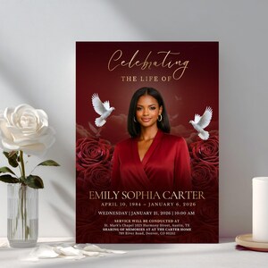 May include: A funeral program featuring a portrait of a woman in a red top, surrounded by red roses and white doves. The text reads Celebrating the life of Emily Sophia Carter, April 10, 1984 &ndash; January 6, 2026, and service details in gold.