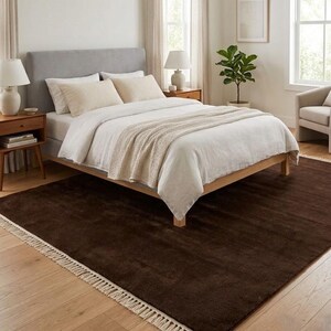Premium chocolate brown hand-knotted rug made of 100% New Zealand wool, featuring a solid contemporary design with contrasting fringed edges, styled under a mid-century coffee table in a modern minimalist living room.