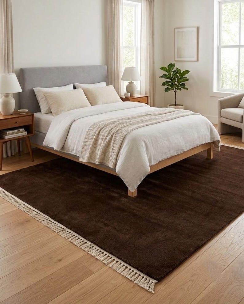 Premium chocolate brown hand-knotted rug made of 100% New Zealand wool, featuring a solid contemporary design with contrasting fringed edges, styled under a mid-century coffee table in a modern minimalist living room.