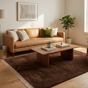 Premium chocolate brown hand-knotted rug made of 100% New Zealand wool, featuring a solid contemporary design with contrasting fringed edges, styled under a mid-century coffee table in a modern minimalist living room.