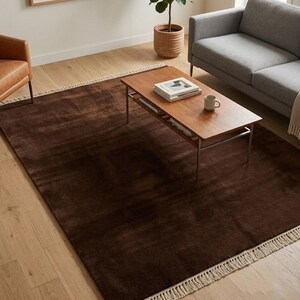 Premium chocolate brown hand-knotted rug made of 100% New Zealand wool, featuring a solid contemporary design with contrasting fringed edges, styled under a mid-century coffee table in a modern minimalist living room.