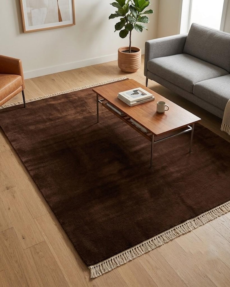 Premium chocolate brown hand-knotted rug made of 100% New Zealand wool, featuring a solid contemporary design with contrasting fringed edges, styled under a mid-century coffee table in a modern minimalist living room.