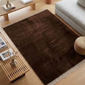 Premium chocolate brown hand-knotted rug made of 100% New Zealand wool, featuring a solid contemporary design with contrasting fringed edges, styled under a mid-century coffee table in a modern minimalist living room.