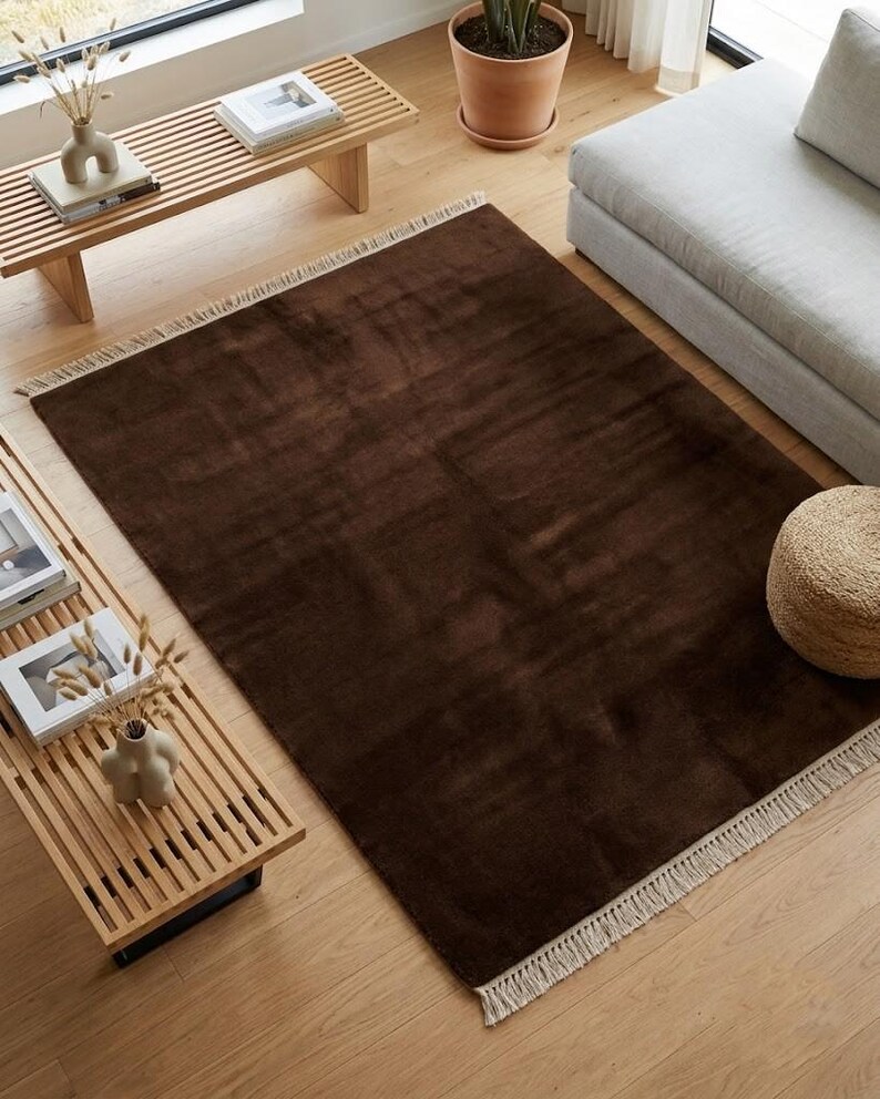 Premium chocolate brown hand-knotted rug made of 100% New Zealand wool, featuring a solid contemporary design with contrasting fringed edges, styled under a mid-century coffee table in a modern minimalist living room.