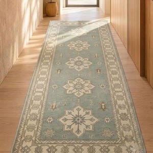 May include: A long rectangular runner rug featuring a light blue field with a repeating pattern of cream-colored geometric floral medallions. The rug is framed by a wide border with intricate cream and blue linear designs and short fringe ends.