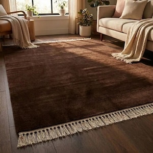 Premium chocolate brown hand-knotted rug made of 100% New Zealand wool, featuring a solid contemporary design with contrasting fringed edges, styled under a mid-century coffee table in a modern minimalist living room.