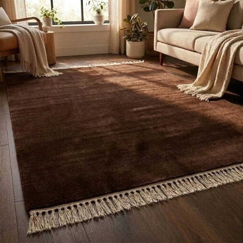 Premium chocolate brown hand-knotted rug made of 100% New Zealand wool, featuring a solid contemporary design with contrasting fringed edges, styled under a mid-century coffee table in a modern minimalist living room.