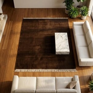 Premium chocolate brown hand-knotted rug made of 100% New Zealand wool, featuring a solid contemporary design with contrasting fringed edges, styled under a mid-century coffee table in a modern minimalist living room.