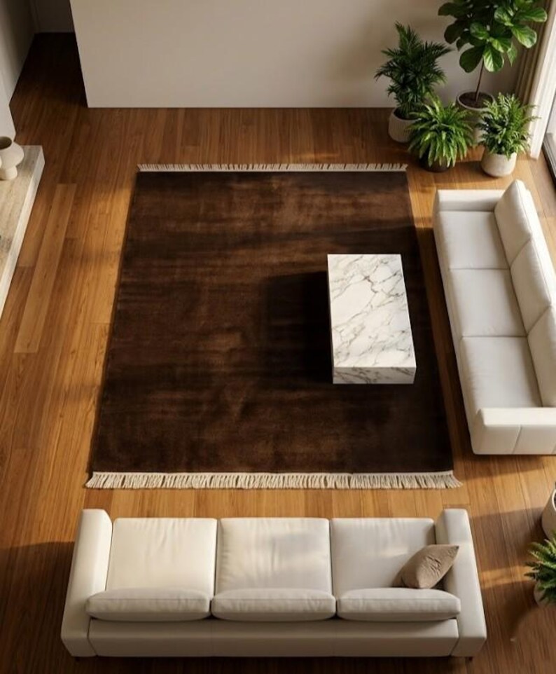 Premium chocolate brown hand-knotted rug made of 100% New Zealand wool, featuring a solid contemporary design with contrasting fringed edges, styled under a mid-century coffee table in a modern minimalist living room.