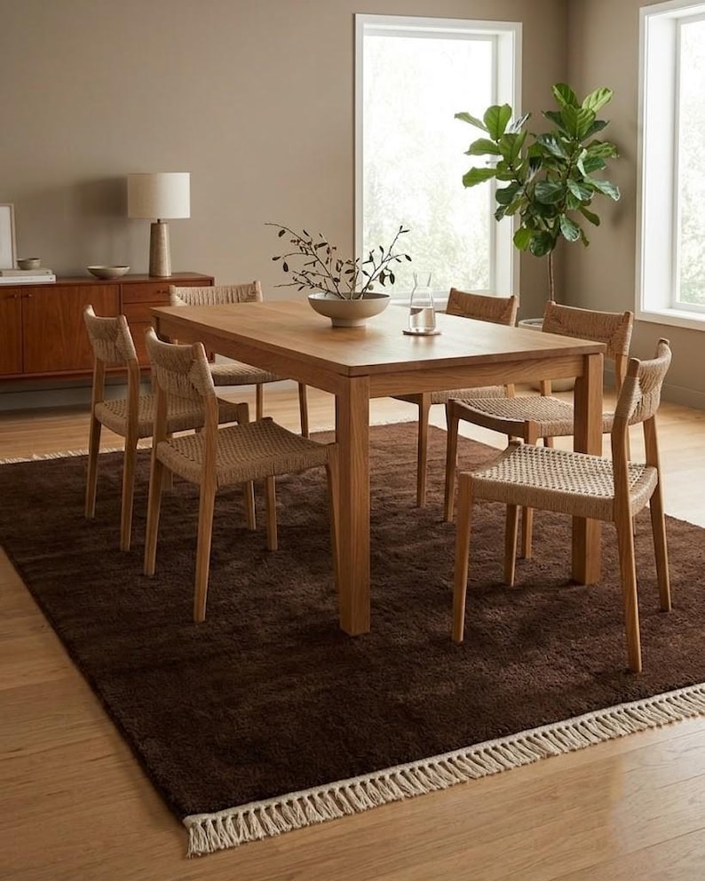 Premium chocolate brown hand-knotted rug made of 100% New Zealand wool, featuring a solid contemporary design with contrasting fringed edges, styled under a mid-century coffee table in a modern minimalist living room.