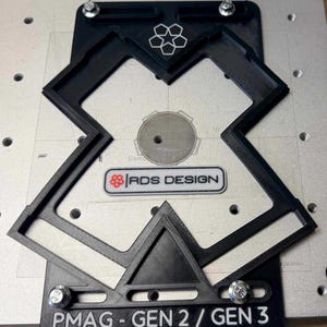 May include: Black plastic jig with the text "PMAG - GEN 2 / GEN 3 AR-15 30 ROUND" and the "RDS DESIGN" logo. The jig is secured with silver bolts and features a geometric design with a pentagon shape.