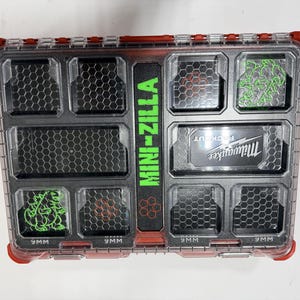 May include: A red and black Milwaukee Packout organizer case with a clear lid. The center features the text MINI-ZILLA in green. Two compartments contain green monster graphics, and several compartments are labeled 9MM at the bottom.