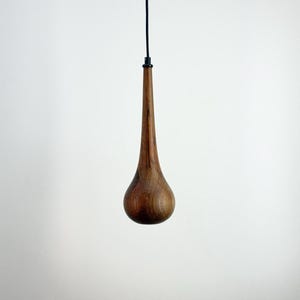 May include: A teardrop-shaped wooden pendant light fixture. The light has a dark brown, polished finish and is suspended from a black cord. The fixture is a modern design, suitable for a minimalist interior.