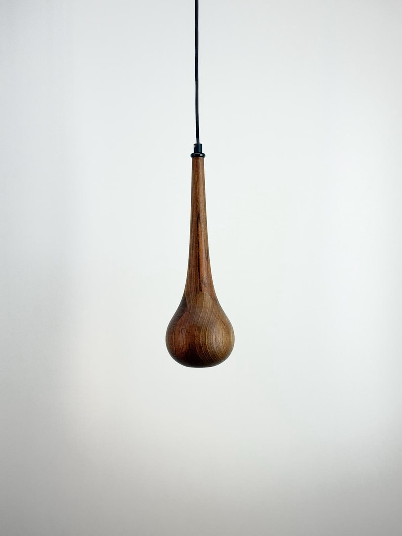 May include: A teardrop-shaped wooden pendant light fixture. The light has a dark brown, polished finish and is suspended from a black cord. The fixture is a modern design, suitable for a minimalist interior.