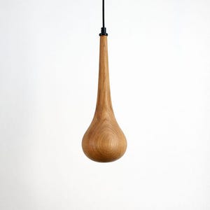 May include: A teardrop-shaped wooden pendant light fixture. The light has a long, slender neck and a rounded base. The wood grain is visible, and the fixture hangs from a black cord.