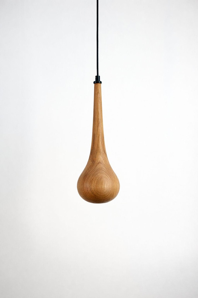 May include: A teardrop-shaped wooden pendant light fixture. The light has a long, slender neck and a rounded base. The wood grain is visible, and the fixture hangs from a black cord.