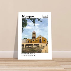 Puede incluir: Una impresión fotográfica de la iglesia Santa Cruz de Mompox en Colombia. La iglesia es amarilla con una torre campanario con techo rojo. La impresión incluye el texto "Mompox" y las coordenadas 9.2397° N, 74.4254° W.